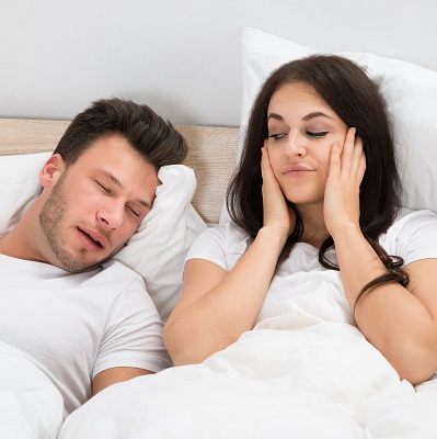 Woman covering ears because of husbands snoring due to sleep apnea.